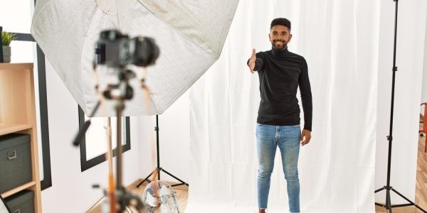 Young hispanic man with beard posing as model at photography studio smiling friendly offering handshake as greeting and welcoming. successful business.